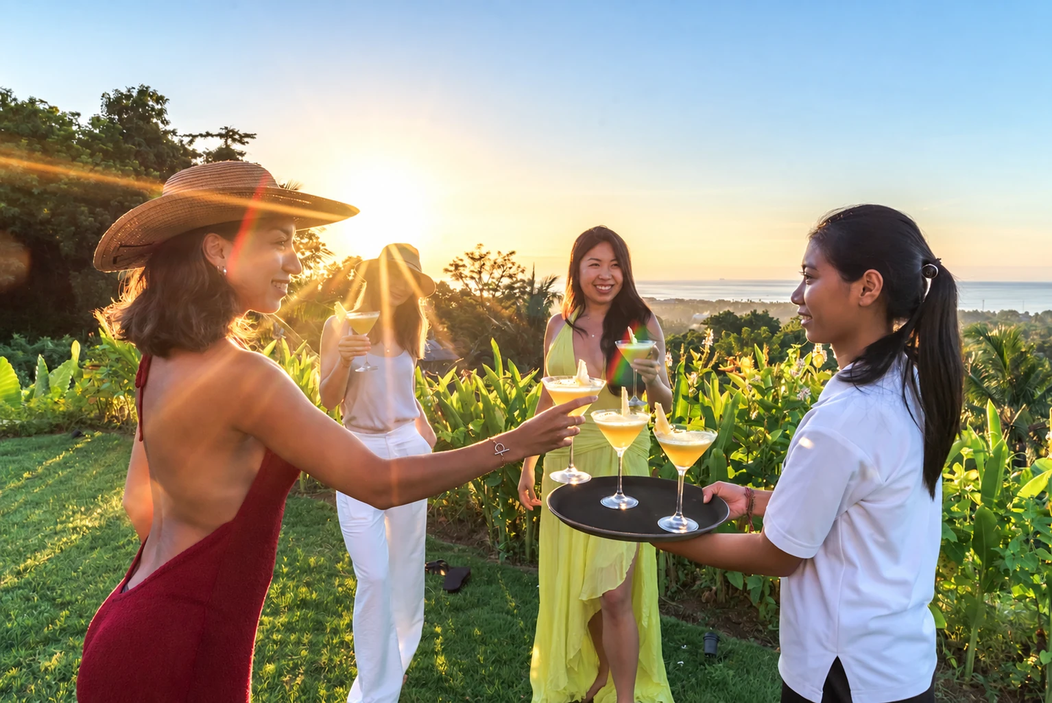 Property guests receiving drinks in garden at sunset; villa staff and guests visible.